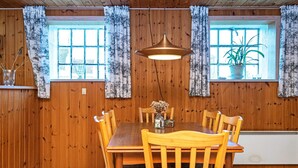 A wooden-paneled dining room with a table and chairs, two windows with curtains, and a hanging light fixture. - 6 Person Holiday Home in Ribe (Ribe)