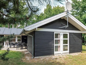 A small, single-story building with a dark exterior, a satellite dish, and a patio area with outdoor furniture.