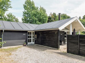 A two-story building with a dark exterior, a covered porch, and a gravel driveway.