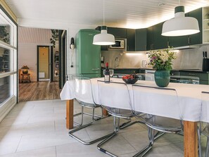 A modern kitchen with a dining area, featuring a table with chairs, a green refrigerator, and pendant lights.