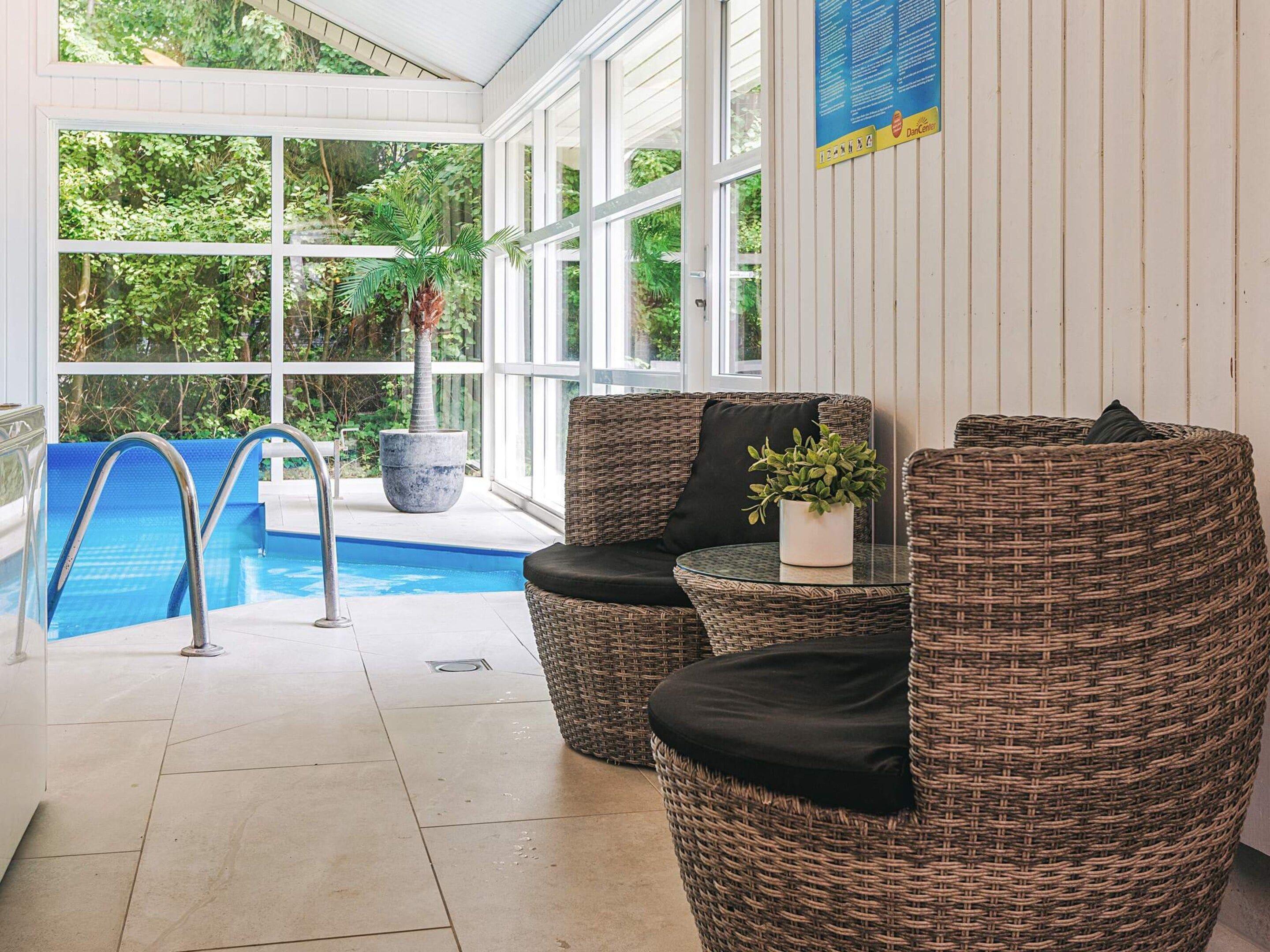 Un espace piscine intérieur aménagé avec des meubles en osier et une plante en pot.
