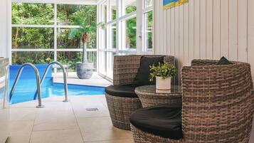 Un espace piscine intérieur aménagé avec des meubles en osier et une plante en pot.