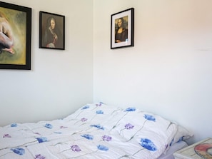 Quarto com cama, travesseiro, mesa de cabeceira e duas fotos emolduradas na parede.
