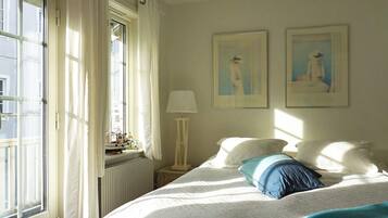 Ein Schlafzimmer mit einem Bett, einem Fenster mit Vorhängen, einem Heizkörper und zwei gerahmten Bildern an der Wand.