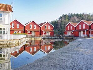 A row of red wooden houses with white trim, a stone wall, and a calm water body reflecting the buildings. - 4 Star Holiday Home in Stromstad (Stromstad)