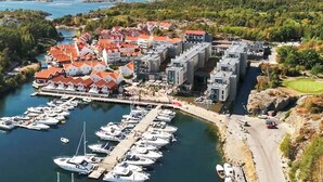 A marina with boats docked, a building complex with red roofs, and a hilly landscape in the background. - 4 Star Holiday Home in Stromstad (Stromstad)