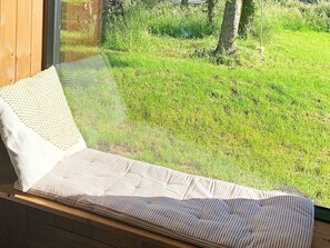 A bed with a striped mattress and a white pillow, positioned next to a window overlooking a grassy yard. - 5 Star Holiday Home in Vinderup (Vinderup)