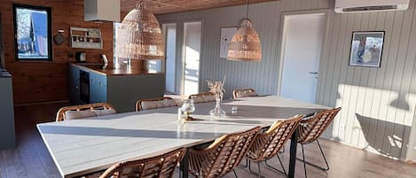 A spacious dining area with a long table and wicker chairs, a kitchen with wooden cabinets, and a hanging light fixture.