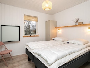 A bedroom with a bed, a chair, a window with blinds, a wall-mounted light, and a hanging light fixture.