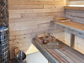 A sauna area with wooden benches, a stone wall, and a metal container labeled 'HARVIA'.