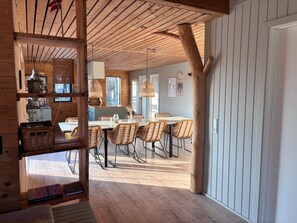 A wooden interior with a dining area, wicker chairs, and a large tree trunk. - 5 Star Holiday Home in Vinderup (Vinderup)