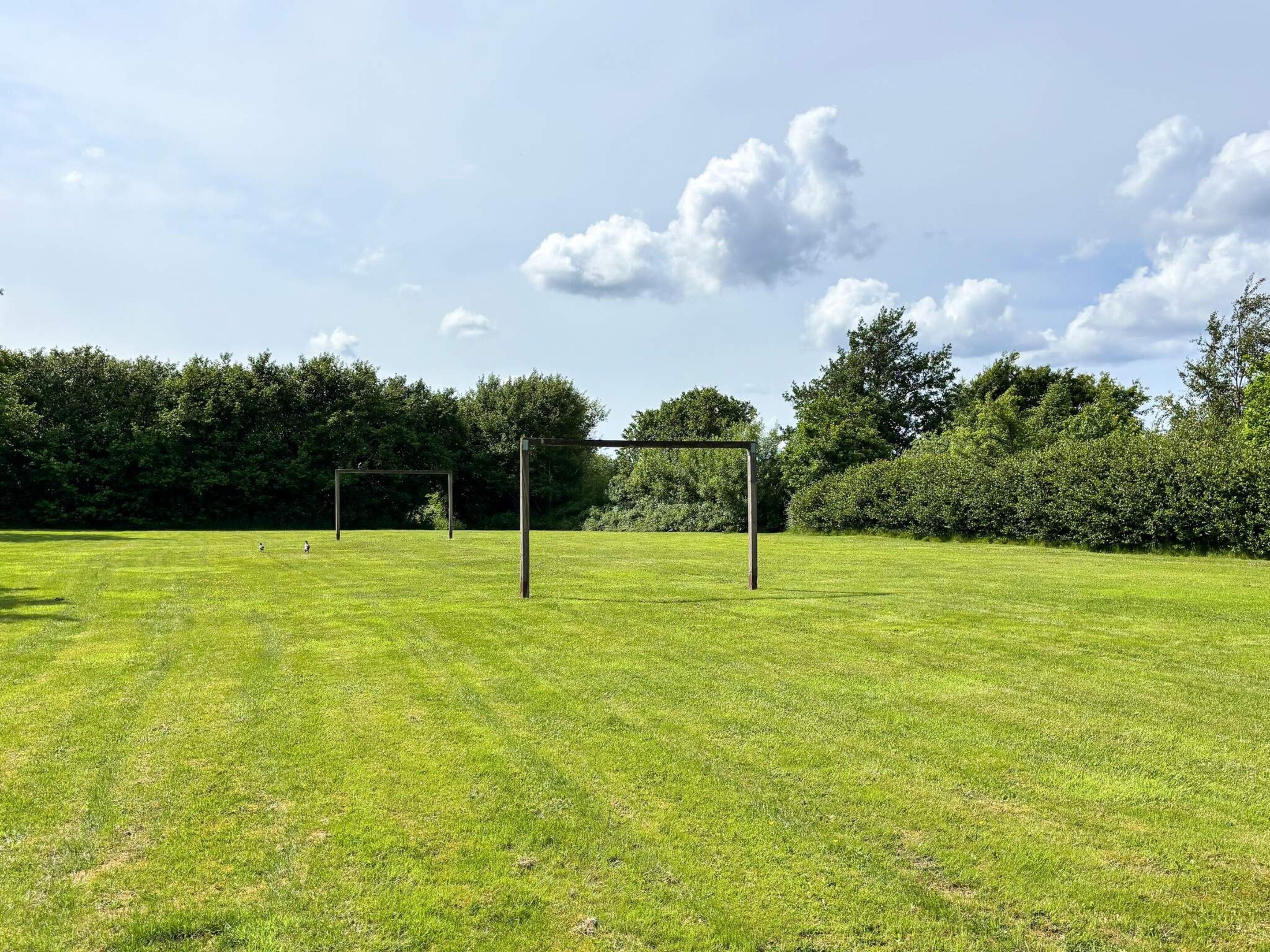 An open grassy field with two metal structures, possibly for sports or activities, surrounded by dense greenery and trees.