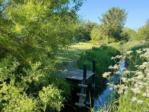 A garden with a wooden bridge over a stream, surrounded by lush greenery and trees.