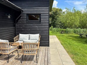 A wooden deck with wicker furniture and a concrete pathway leading to a grassy area. - 5 Star Holiday Home in Vinderup (Vinderup)