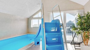 En inomhuspool med en blå vattenrutschkana, en stege och en krukväxt.