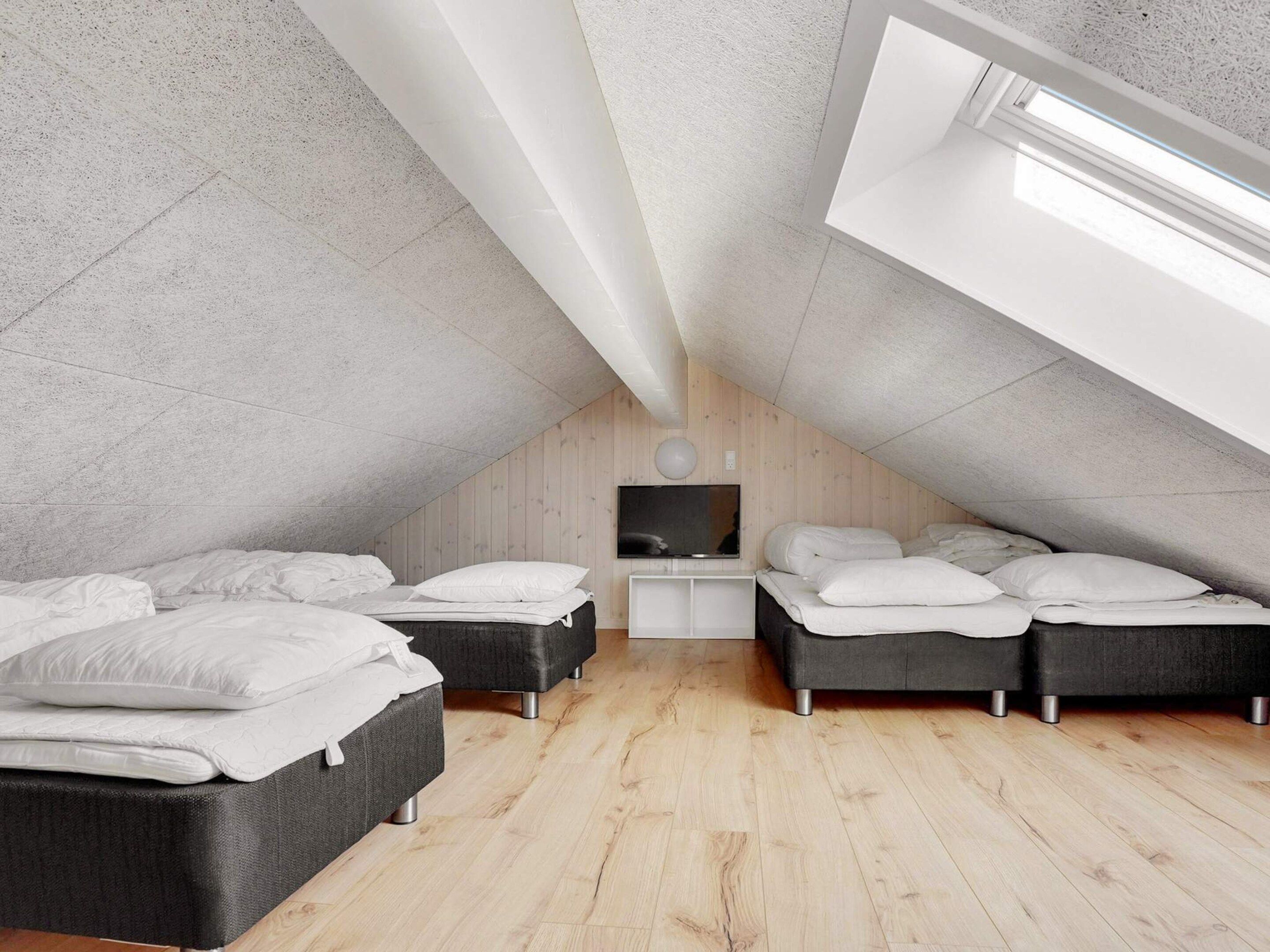 A modern attic bedroom with two beds, a TV, and a skylight.
