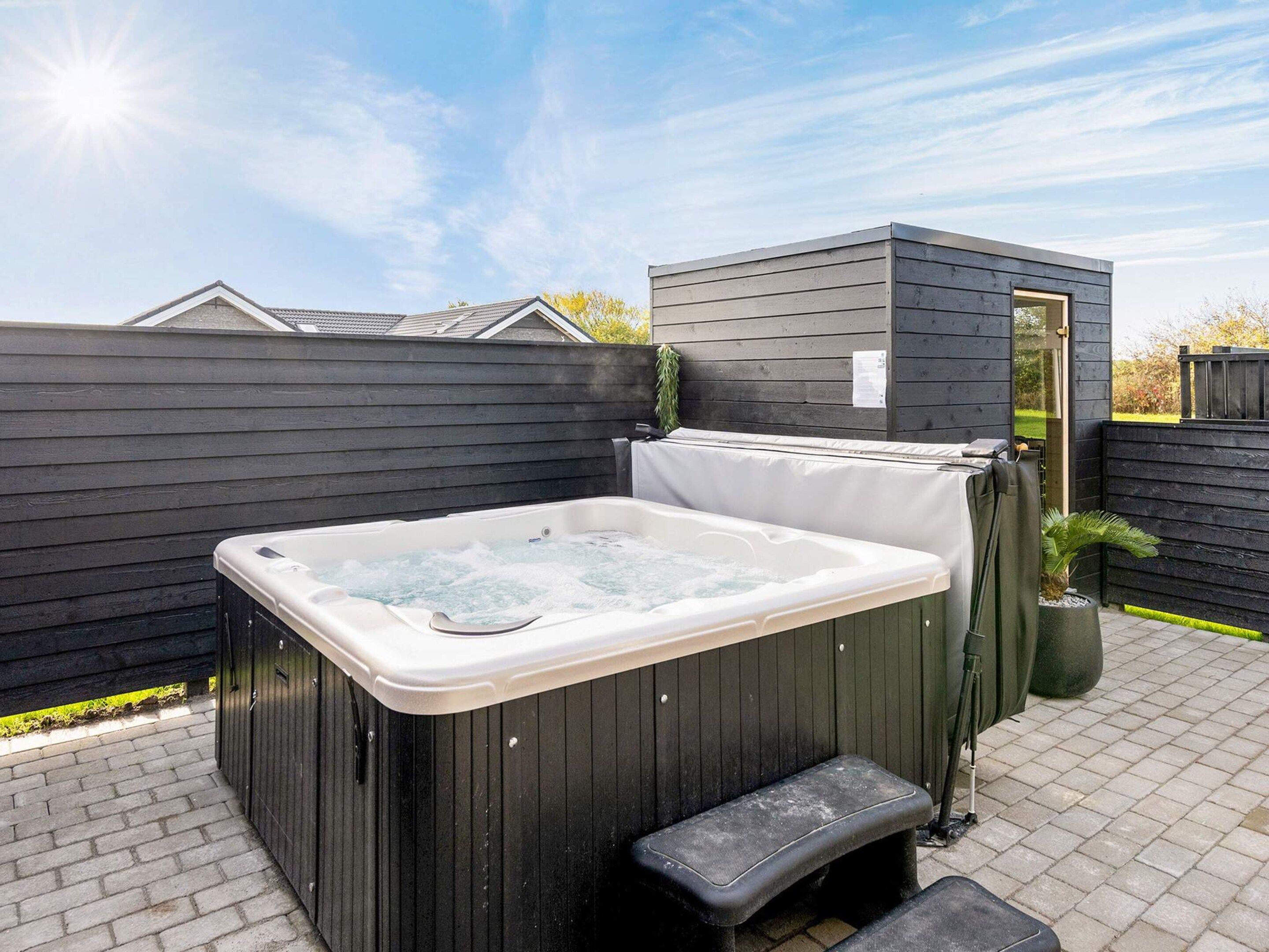 A hot tub with a bench, surrounded by a wooden fence and a small shed.
