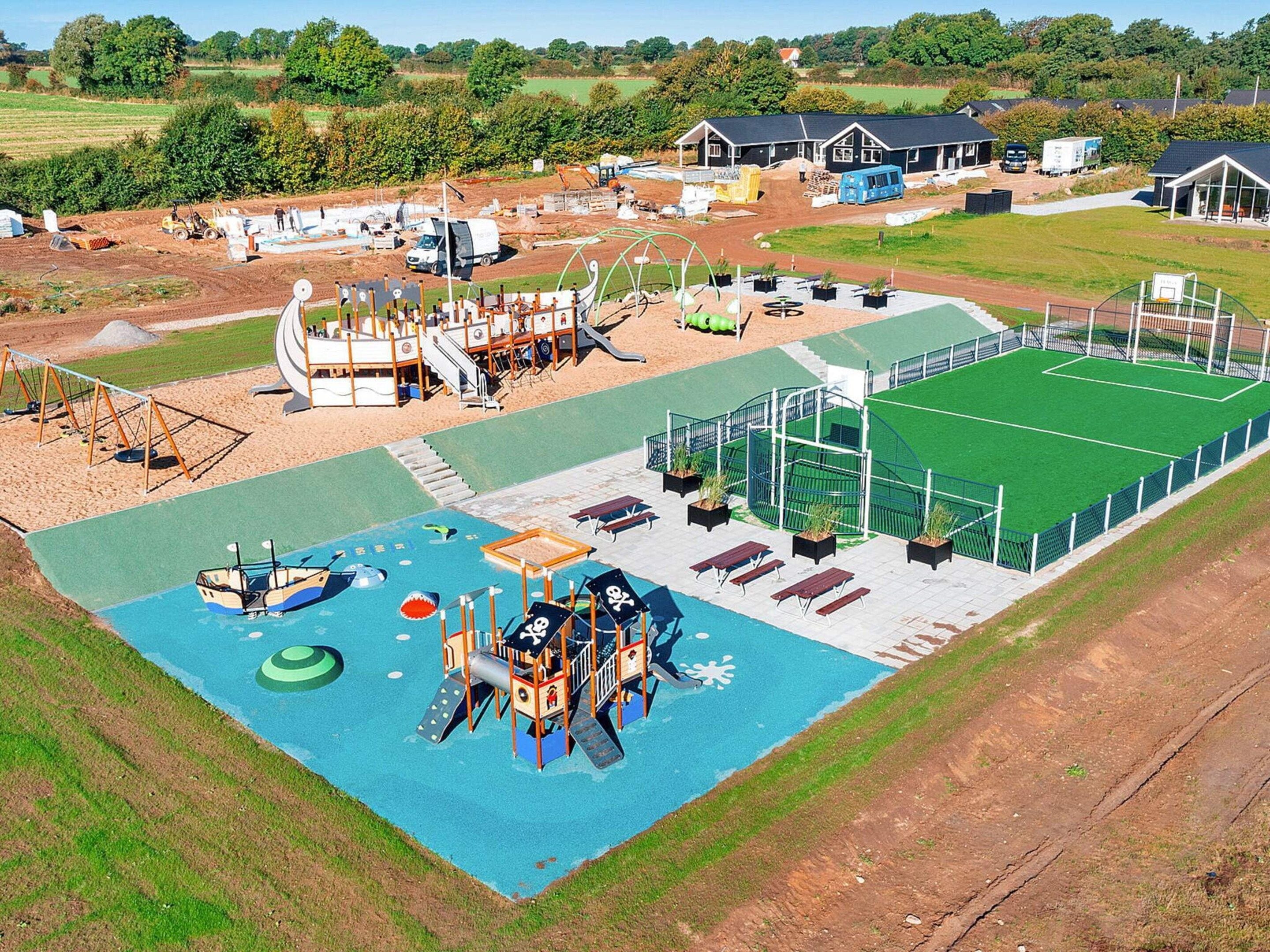 An aerial view of a playground with various play structures, a small pool, and a fenced sports field.