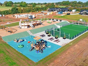 An aerial view of a playground with various play structures, a small pool, and a fenced sports field.