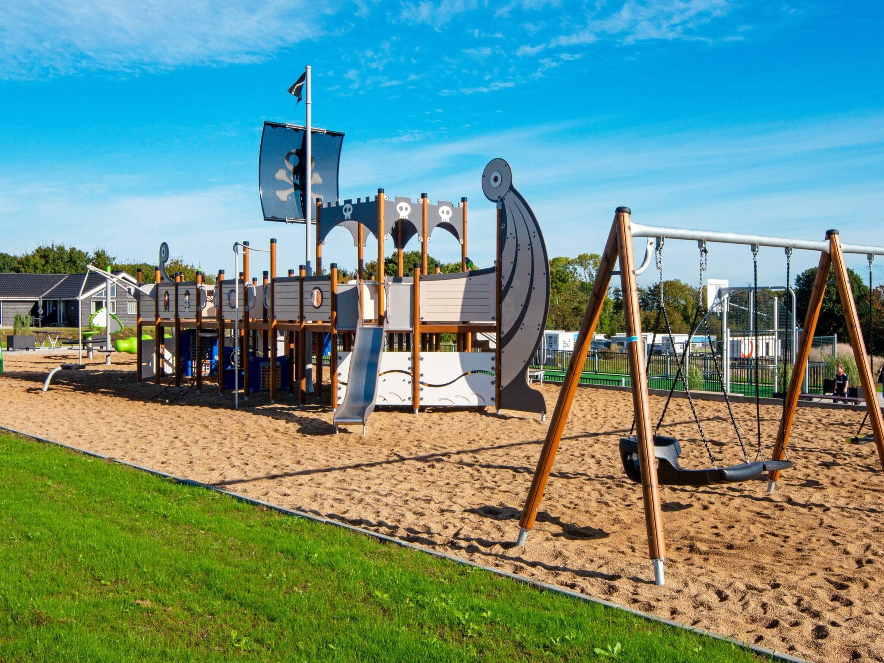 A playground with a ship-themed play structure, swings, and a sand area.