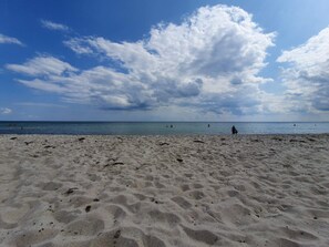 A sandy beach with footprints and a few people in the water.