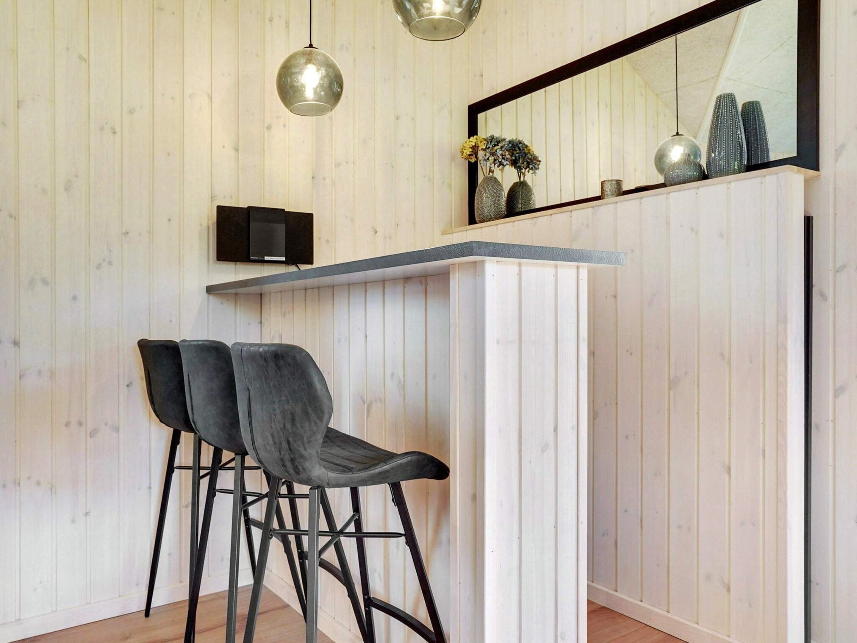 Een moderne keuken met een houten wand, een bar, twee barkrukken, hanglampen en een grote spiegel.
