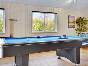 A pool table with a blue felt surface, positioned in a room with wooden panel walls and large windows.