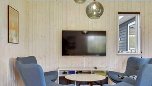 A living room with two blue armchairs, a round table, a flat-screen TV, wooden panel walls, and a window with a view. - 5 Star Holiday Home in Sydals (Sydals)