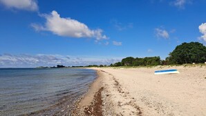 A beach with a clear sky, a sandy shore, and a blue and white surfboard on the sand. - 5 Star Holiday Home in Sydals (Sydals)