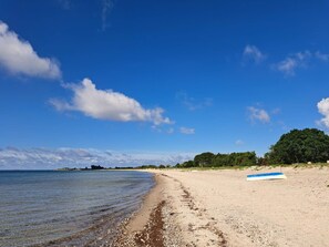 A beach with a clear sky, a sandy shore, and a blue and white surfboard on the sand. - 5 Star Holiday Home in Sydals (Sydals)