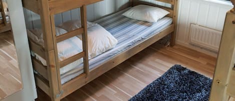 Un lit superposé avec une fenêtre au-dessus, un plancher en bois et un tapis bleu.