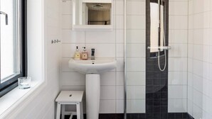 Un bagno con lavandino bianco, uno specchio sopra, una doccia con porta in vetro e un piccolo sgabello bianco.