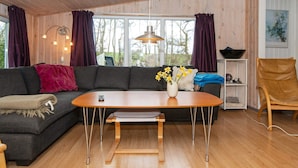 A modern living room with a wooden ceiling, a dark grey sectional sofa, a wooden coffee table, and a vase with yellow flowers. - 10 Person Holiday Home in Ronde (Ronde)