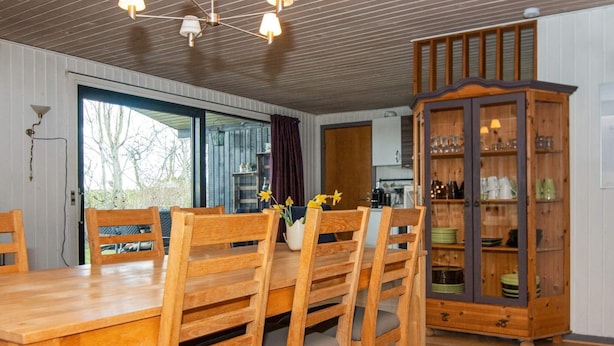 A dining area with a wooden table and chairs, a cabinet with glass doors, and a view of the outdoors. - 10 Person Holiday Home in Ronde (Ronde)