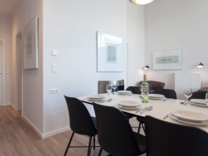 A modern dining area with a white table set for four, black chairs, and a bottle of wine. - 5 Star Holiday Home in Wendtorf (Wendtorf)