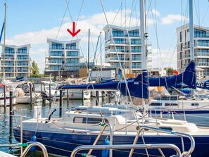 Una marina amb vaixells amarrats, un edifici modern amb balcons i un cel serè.
