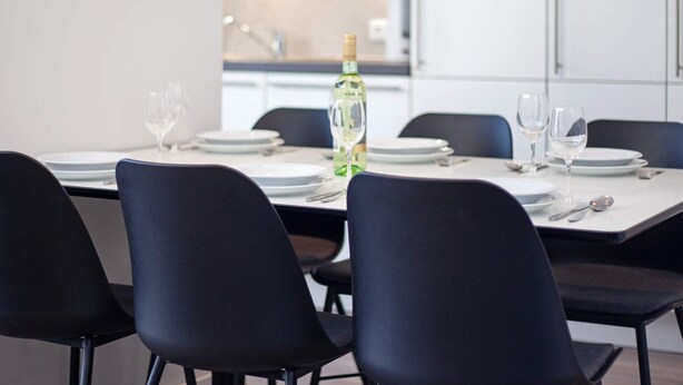 A modern dining area with a table set for four, chairs, and a bottle of white wine.