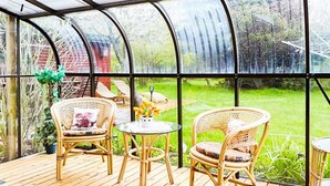 A greenhouse with a wooden deck, wicker chairs, and a glass table. - 6 Person Holiday Home in Gorlev (Gørlev)