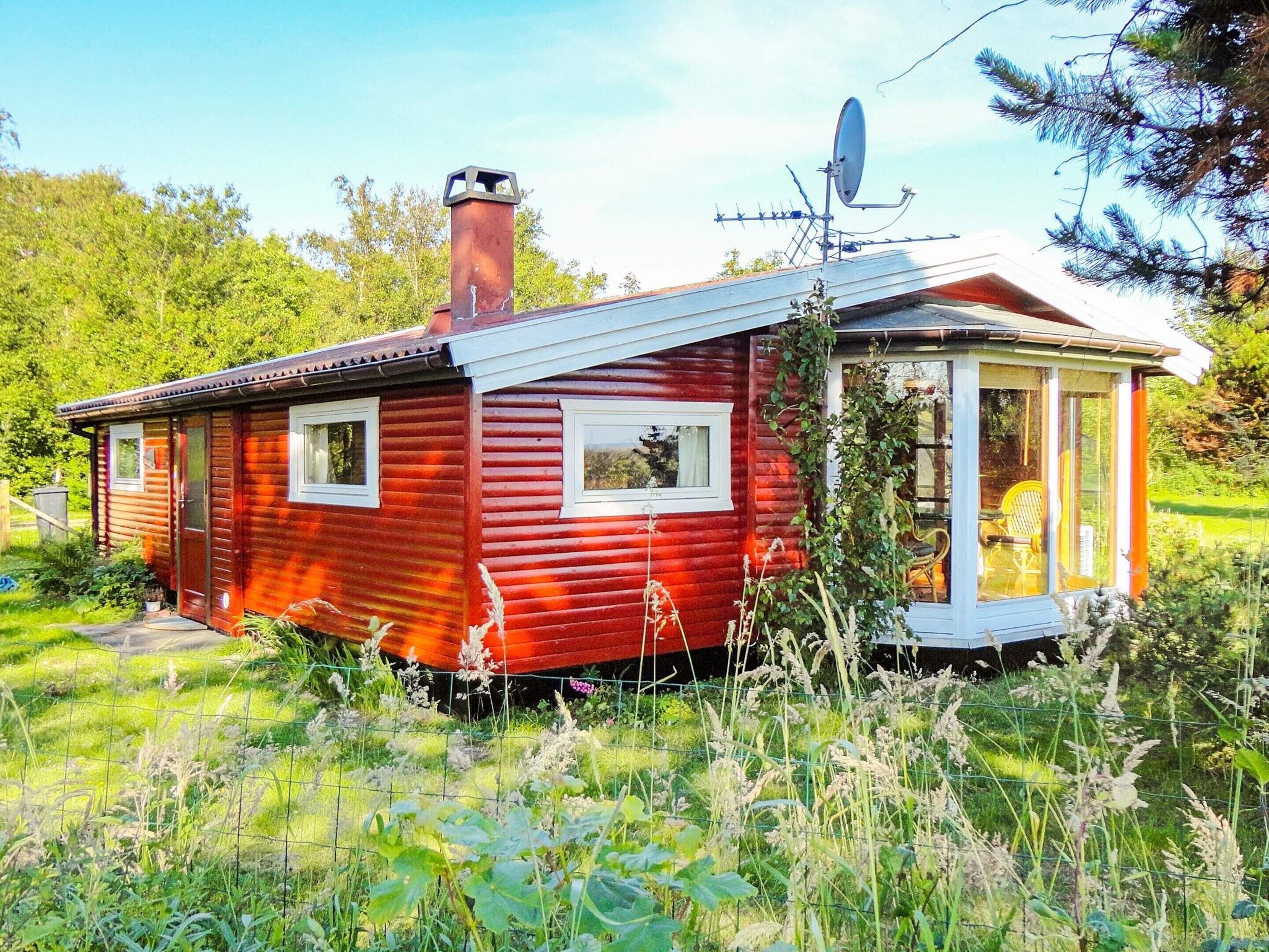 A small, red wooden cabin with a chimney, a satellite dish, and a glass door leading to a porch.