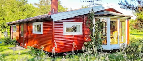 A small, red wooden cabin with a chimney, a satellite dish, and a glass door leading to a porch.