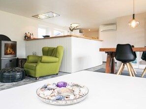 A modern kitchen with a central island, a dining area with a table and chairs, and a living space with a green armchair. - 6 Person Holiday Home in Blokhus (Blokhus)