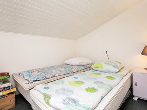 A small, single-bed room with a white ceiling and walls, a bedside table with a lamp, and a stack of books on the floor. - 6 Person Holiday Home in Blokhus (Blokhus)