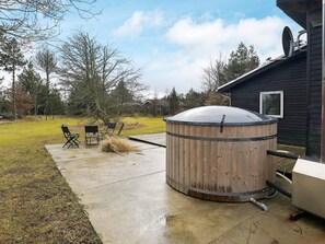 A wooden hot tub with a metal frame, a concrete patio, and a small deck with chairs. - 6 Person Holiday Home in Blokhus (Blokhus)