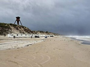 A beach with a lifeguard tower, beach huts, and a sandy shoreline. - 6 Person Holiday Home in Blokhus (Blokhus)
