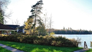A lakeside property with a paved walkway, a house with a covered porch, and a view of the lake. - 2 Person Holiday Home in Bengtsfors-by Traum (Bengtsfors)