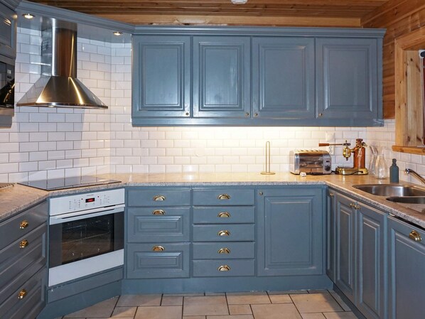 Una cocina con gabinetes azules, una campana extractora de acero inoxidable, un horno empotrado y una encimera con un tostador y una cafetera.
