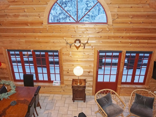 A log cabin interior with a dining area, two windows with red frames, a wall-mounted light fixture, and a decorative antler. - 4 Star Holiday Home in Salen (Salen)