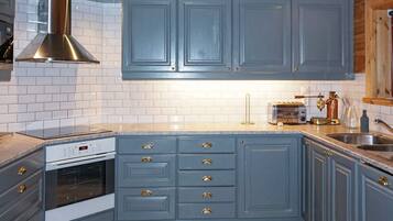 A kitchen with blue cabinets, a stainless steel range hood, a built-in oven, and a countertop with a toaster and a coffee maker.
