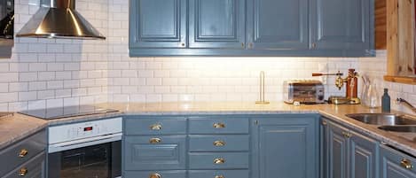 A kitchen with blue cabinets, a stainless steel range hood, a built-in oven, and a countertop with a toaster and a coffee maker.