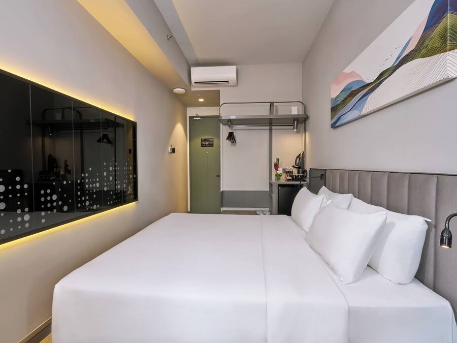 Ein modernes Hotelzimmer mit einem großen Bett, einem fest eingebauten Schreibtisch, einem Spiegel und einem Gemälde an der Wand.